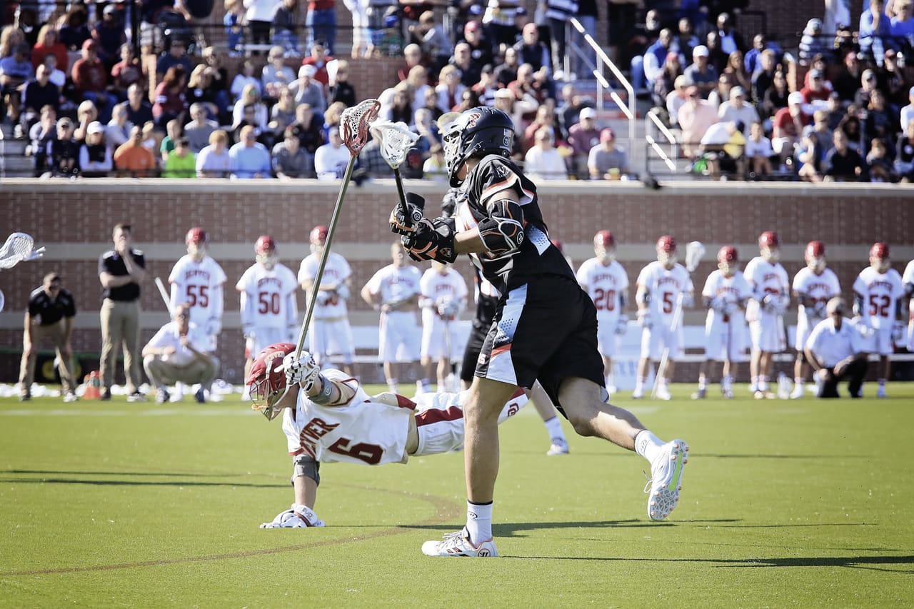 A lacrosse attacker driving past a defender to shoot during a college match.